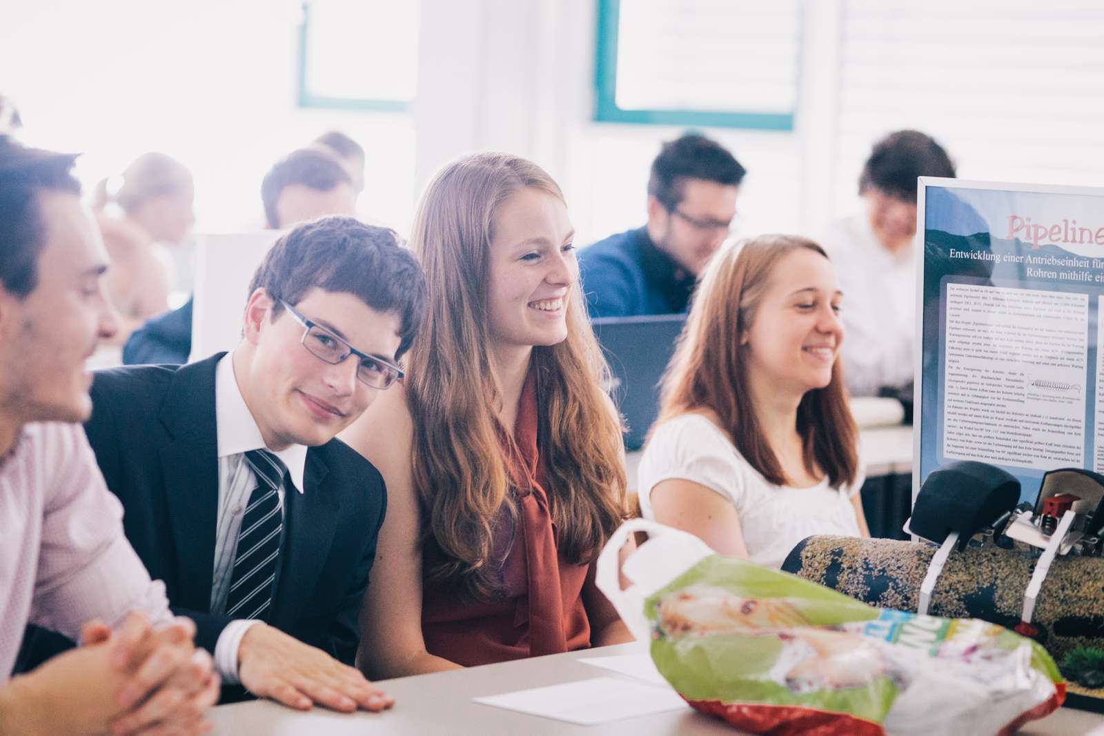 Student im Anzug und Studentinnen lauschen begeistert einem Vortrag