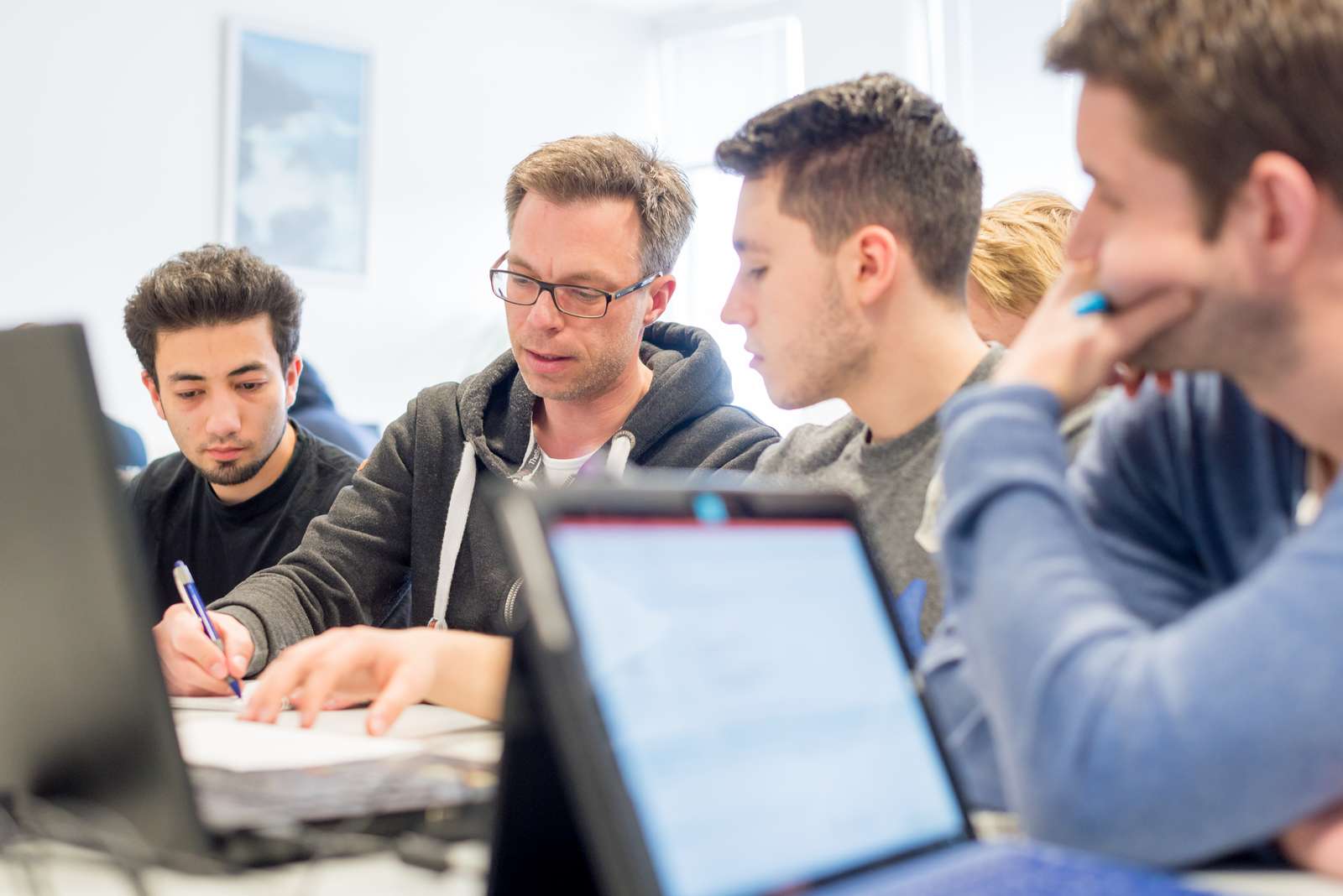 Dozent im Gespräch mit Studierenden, die einen Laptop vor sich haben